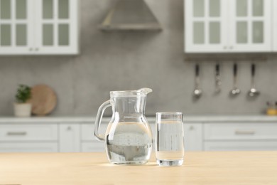 Glass and jug with water on wooden table in kitchen