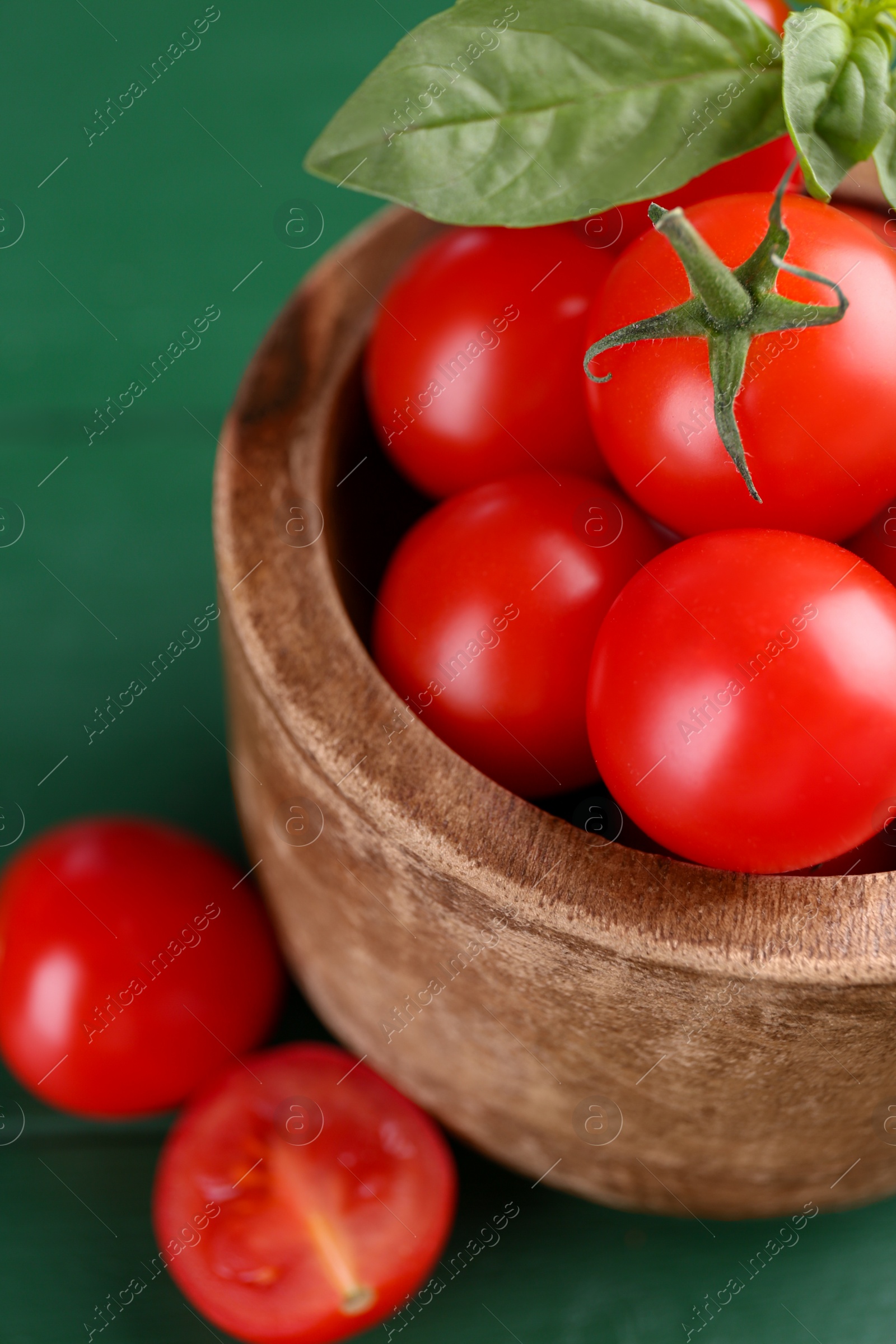 Photo of Ripe tomatoes in wooden bowl on green table, closeup