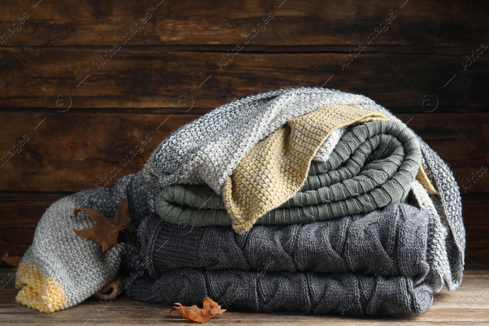 Photo of Stack of knitted plaids with dry leaves on wooden table, closeup