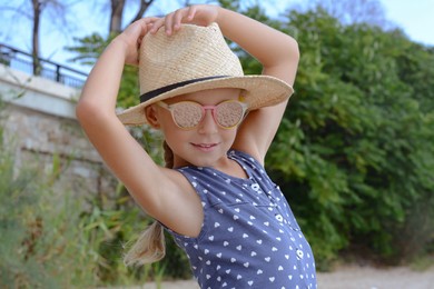 Little girl wearing sunglasses and hat at beach on sunny day