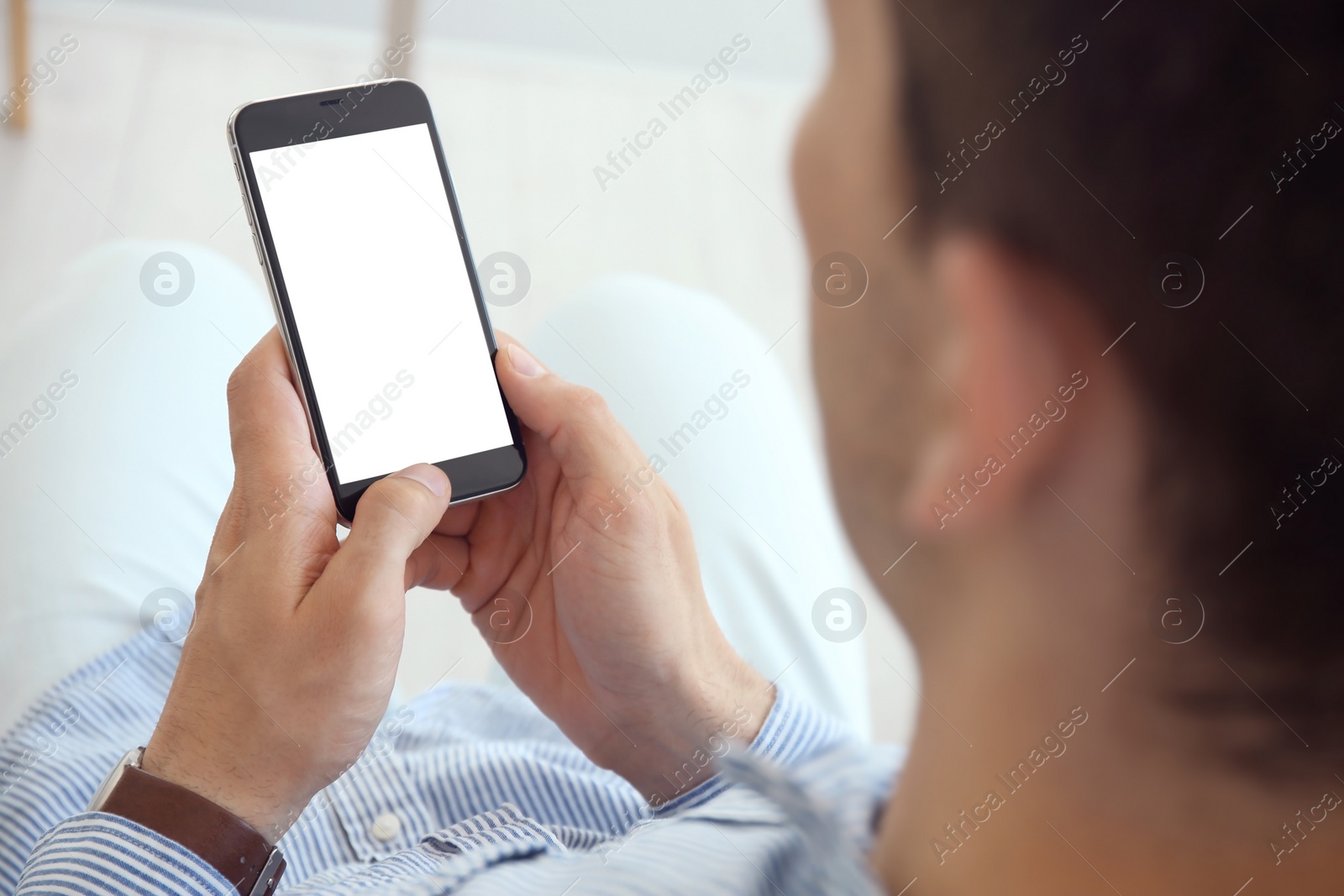 Photo of Young man holding mobile phone with blank screen in hands, indoors