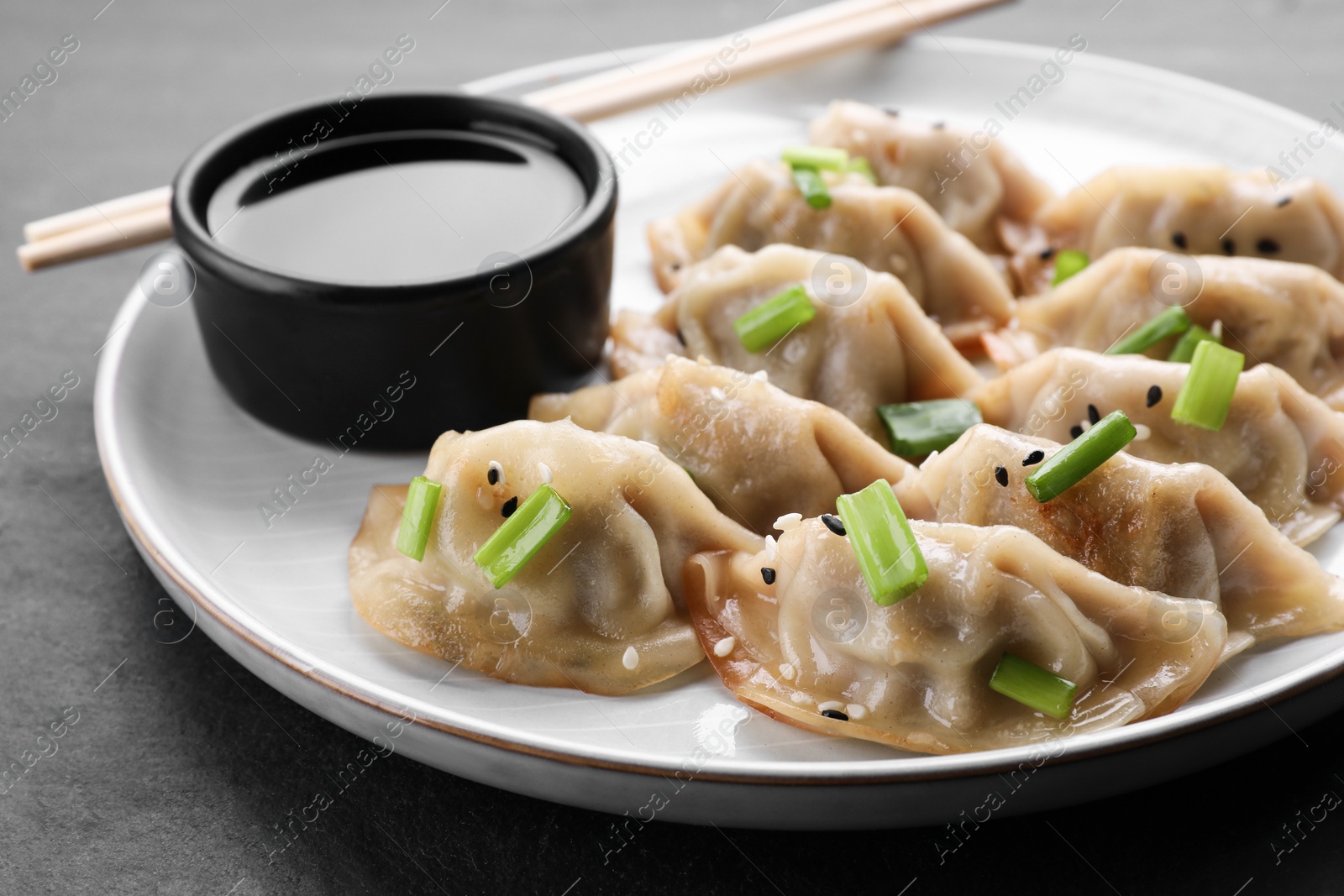 Photo of Delicious gyoza (asian dumplings) with green onions, soy sauce and chopsticks on gray table, closeup