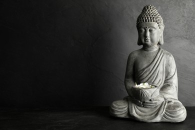 Photo of Buddha statue with petals on black table. Space for text