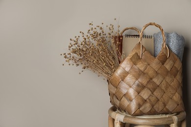 Stylish straw bag with beautiful dried flowers on chair near grey wall, space for text