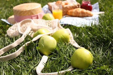 Photo of Fresh apples near blanket with juice and croissant on green grass. Picnic season