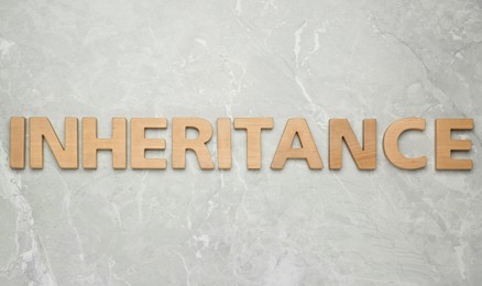 Photo of Word Inheritance made with wooden letters on light marble background, flat lay