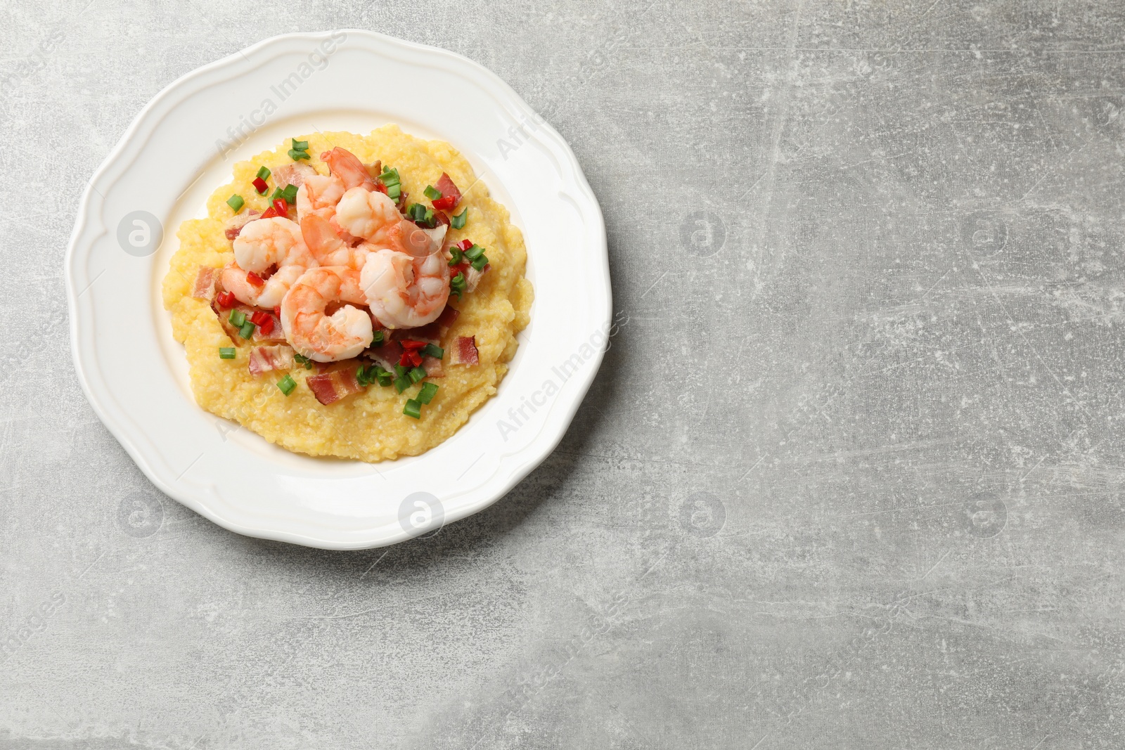 Photo of Plate with fresh tasty shrimps, bacon, grits, green onion and pepper on gray textured table, top view. Space for text