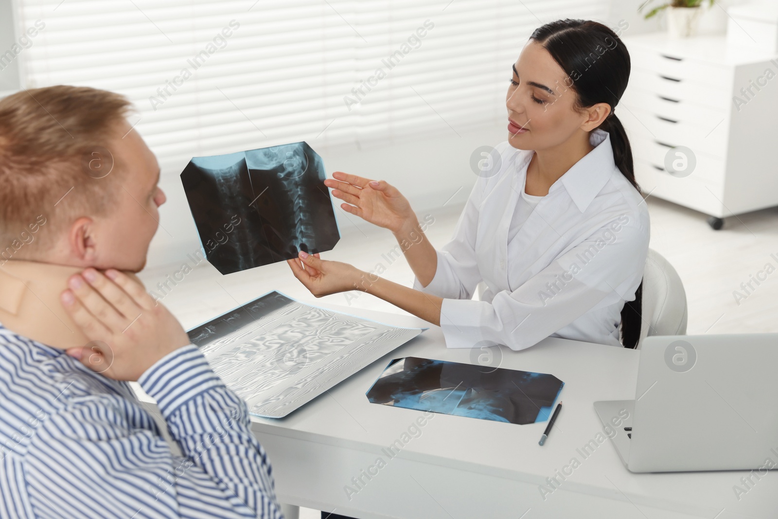 Photo of Doctor with neck MRI image consulting patient in clinic