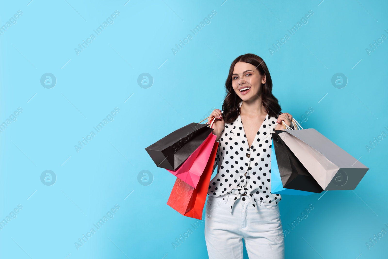 Photo of Beautiful young woman with paper shopping bags on light blue background. Space for text