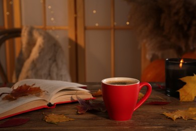 Cup of aromatic coffee, book, candle and autumn leaves on wooden table indoors, space for text