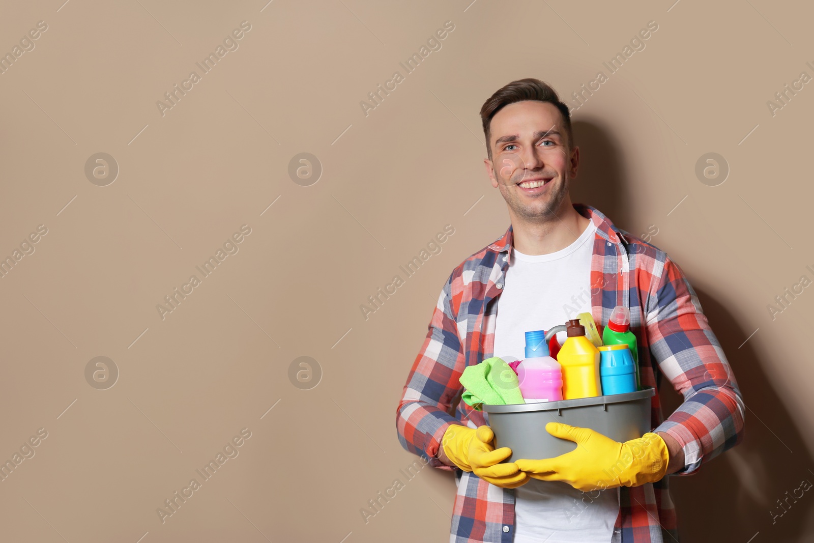 Photo of Man with basin of detergents on color background. Space for text