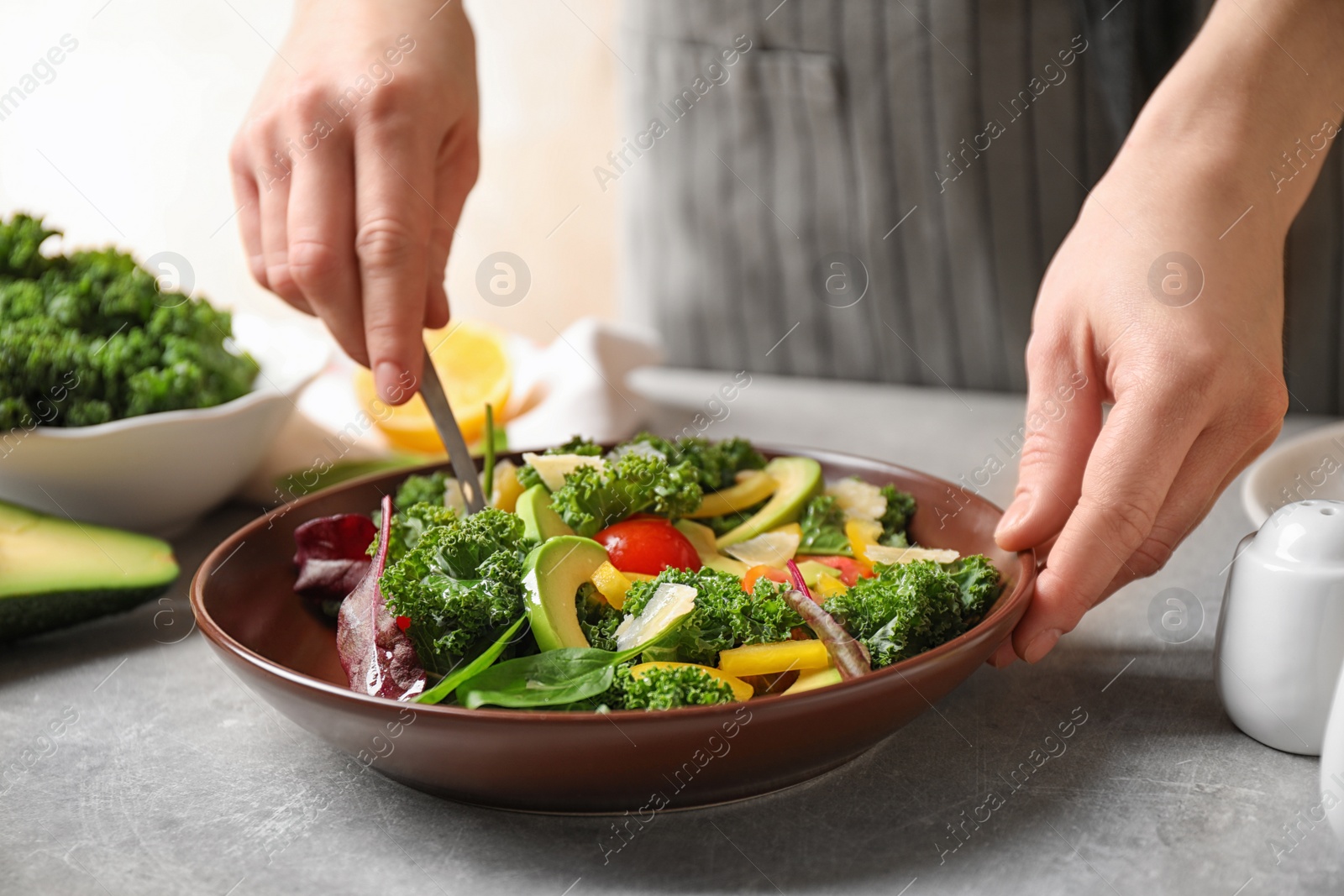 Photo of Woman cooking tasty kale salad on light grey table, closeup