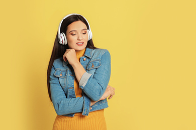 Young woman listening to audiobook on yellow background. Space for text