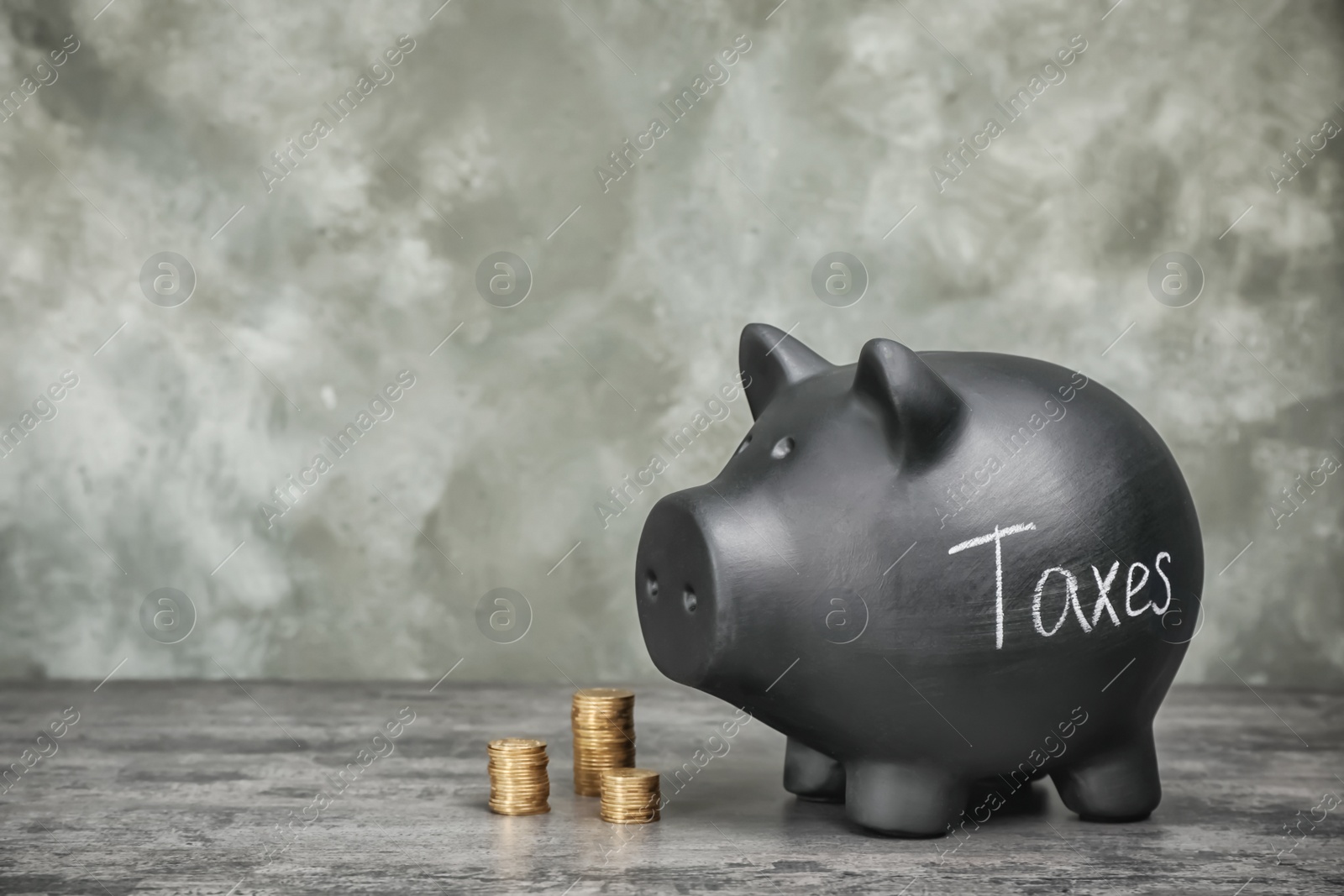 Photo of Black piggy bank with word TAXES and coins on table