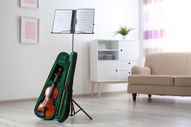 Photo of Violin in case and note stand with music sheets in room