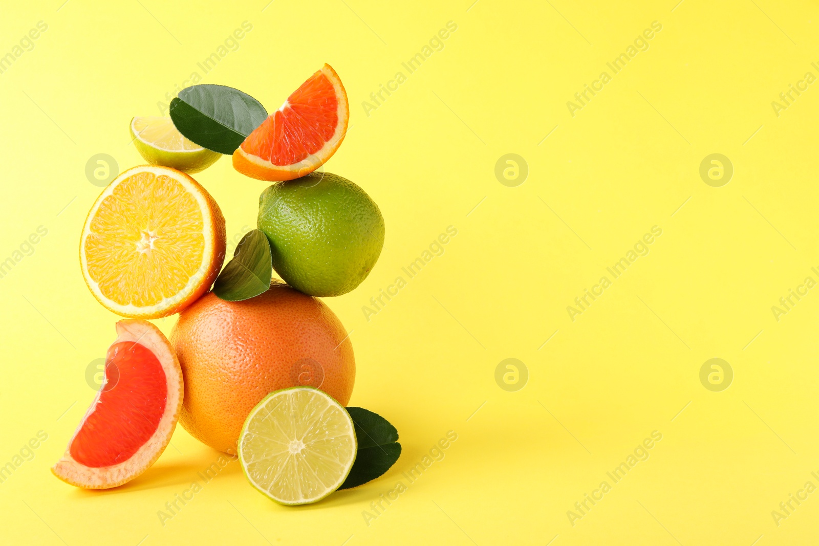 Photo of Fresh ripe citrus fruits and green leaves on yellow background, space for text