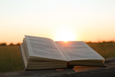 Photo of Open book on wooden bench in field at sunset