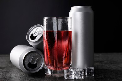 Photo of Energy drink in glass, aluminium cans and ice cubes on grey table, closeup