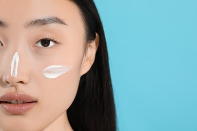 Beautiful young woman with sun protection cream on her face against light blue background, closeup. Space for text