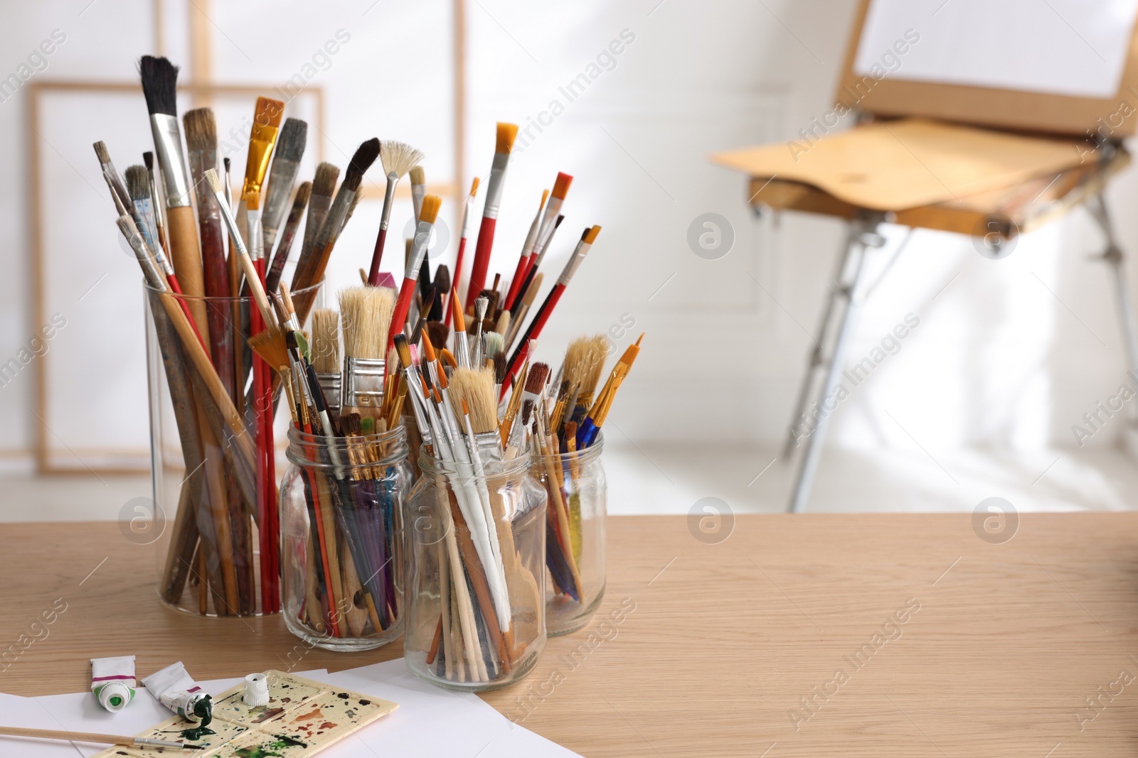 Photo of Different brushes, paints and palette on wooden table indoors, space for text. Artist's workplace