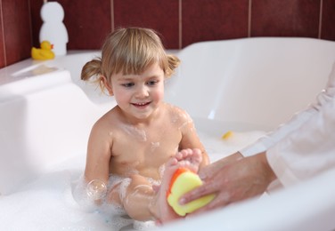 Photo of Mother washing her smiling daughter with sponge in bathtub, closeup