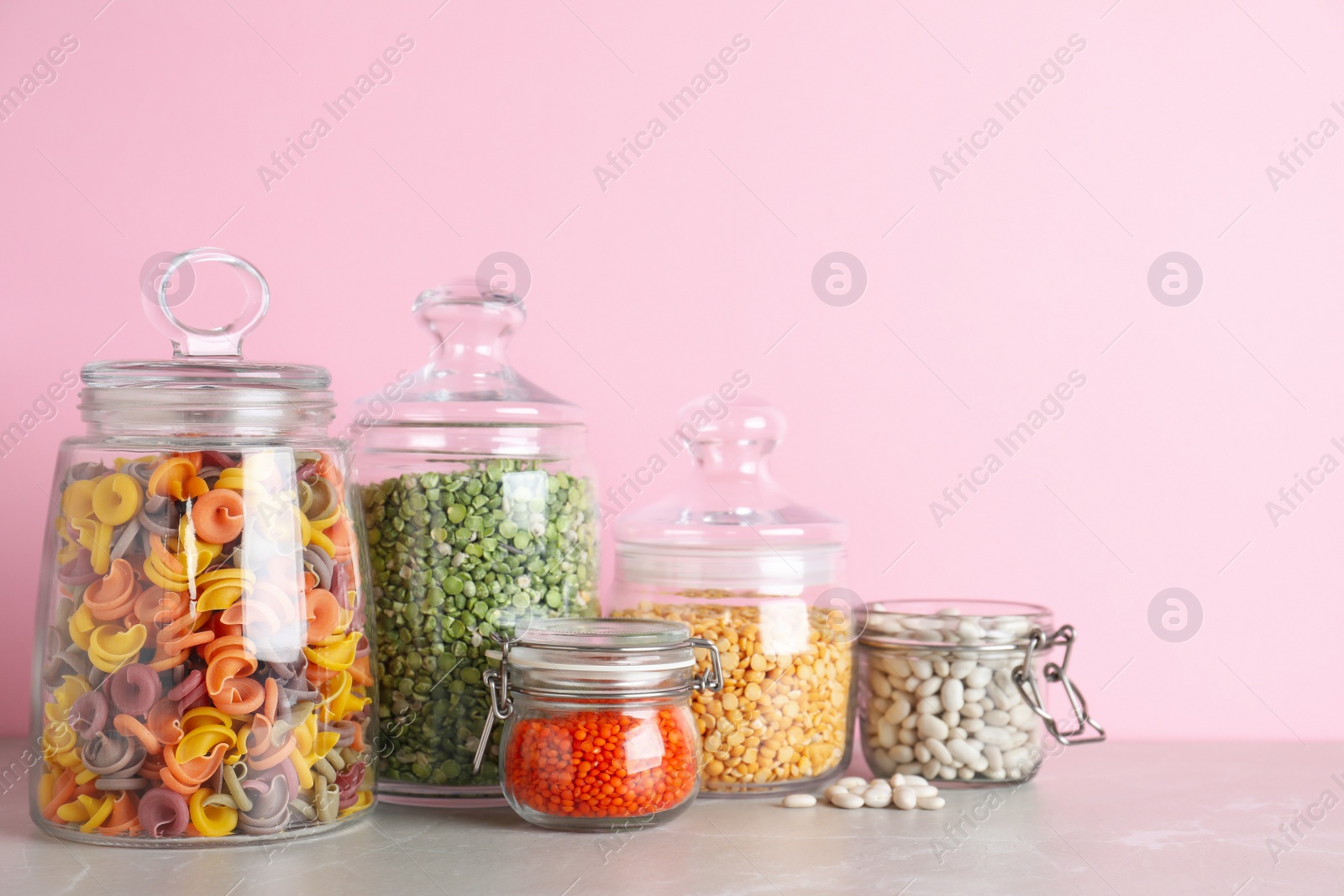 Photo of Glass jars with different types of groats and pasta on light grey marble table