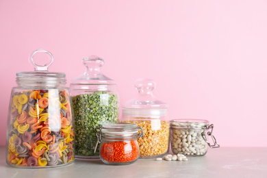 Glass jars with different types of groats and pasta on light grey marble table