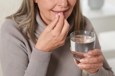 Photo of Senior woman with glass of water taking pill at home, closeup