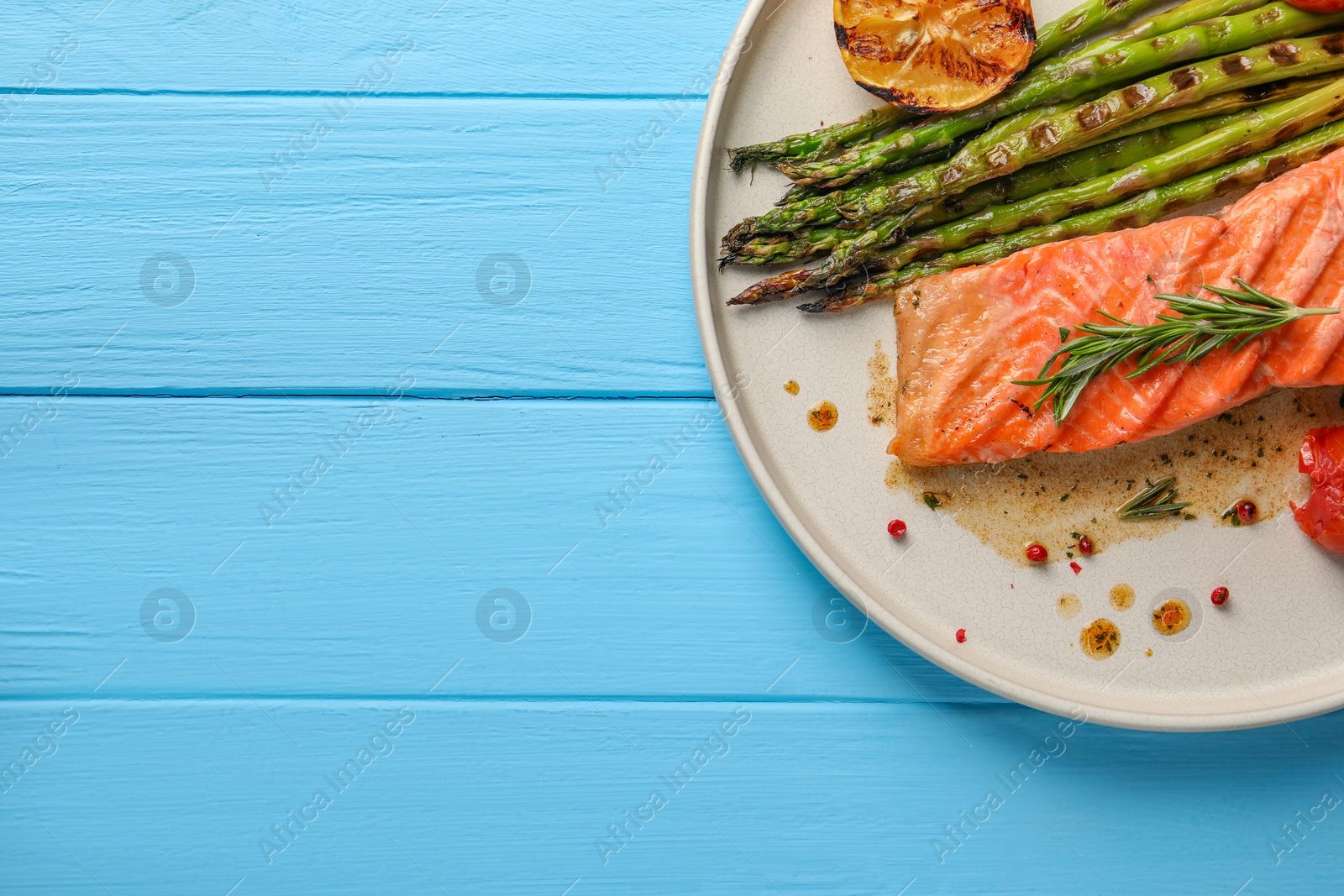 Photo of Tasty grilled salmon with asparagus, lemon and spices on light blue wooden table, top view. Space for text