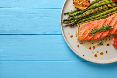 Tasty grilled salmon with asparagus, lemon and spices on light blue wooden table, top view. Space for text