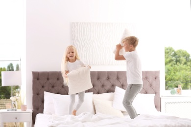 Happy children having pillow fight on bed at home