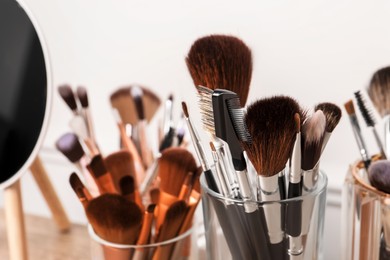 Set of professional makeup brushes and mirror on wooden table, closeup