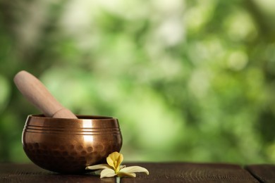 Golden singing bowl, mallet and flower on wooden table outdoors, space for text