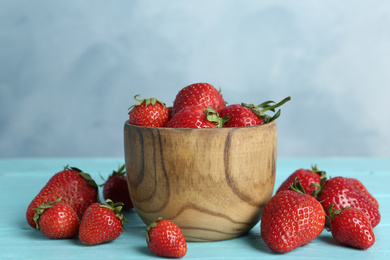 Photo of Delicious ripe strawberries in bowl on light blue wooden table