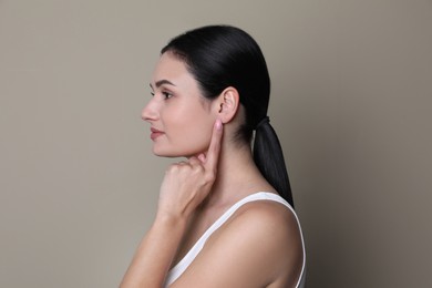 Young woman pointing at her ear on grey background