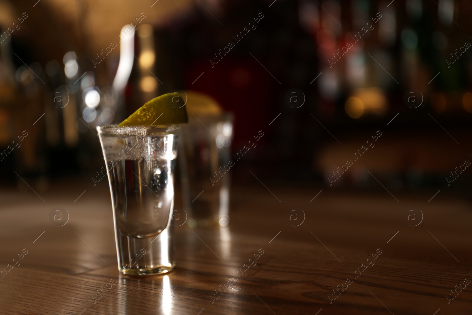 Photo of Tequila shot with lime on wooden counter in bar, space for text. Alcoholic cocktail