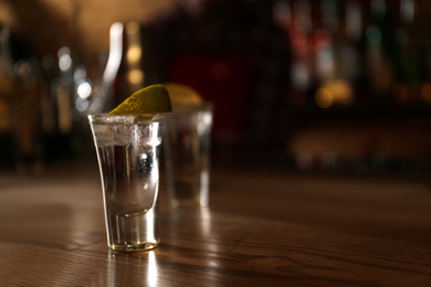 Photo of Tequila shot with lime on wooden counter in bar, space for text. Alcoholic cocktail