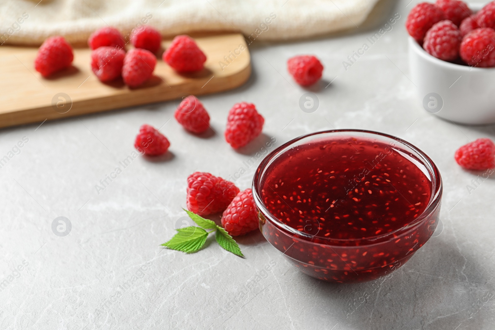 Photo of Bowl of sweet jam with ripe raspberries on white table. Space for text