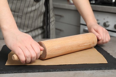 Photo of Woman rolling dough with wooden pin at table in kitchen, closeup