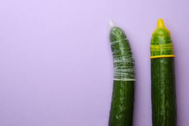 Photo of Cucumbers with condoms on lilac background, flat lay and space for text. Safe sex