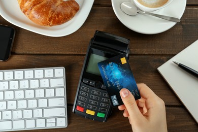 Photo of Woman with credit card using modern payment terminal at wooden table, top view
