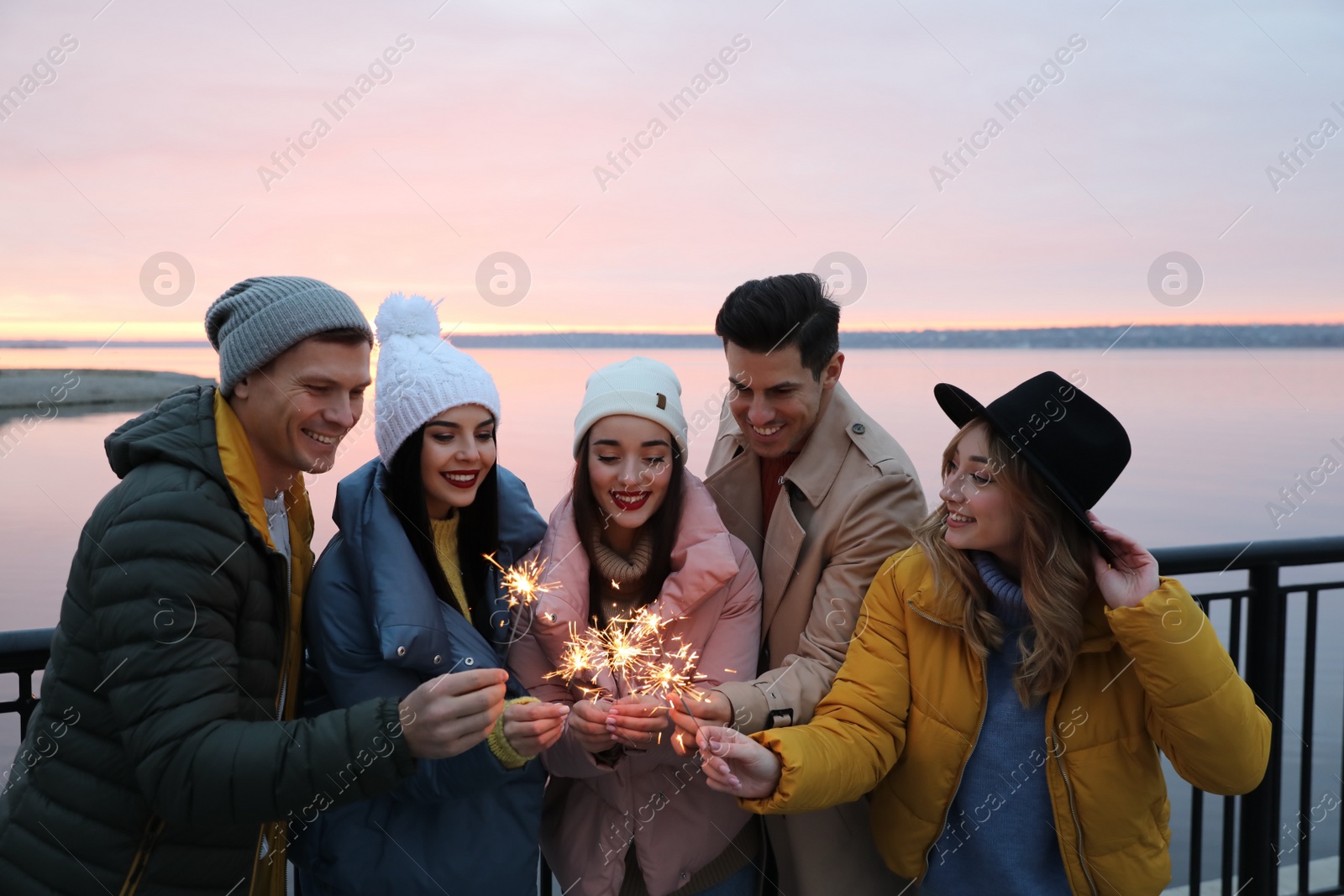 Photo of People in warm clothes holding burning sparklers near river