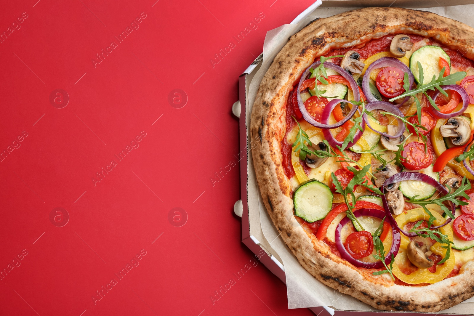 Photo of Delicious vegetable pizza in cardboard box on red background, top view. Space for text