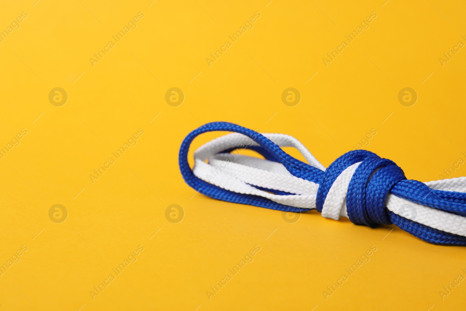 Photo of White and blue shoe laces tied in knot on yellow background. Space for text