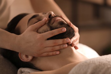 Young man receiving facial massage in beauty salon, closeup