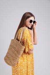 Beautiful young woman with stylish straw bag on light grey background