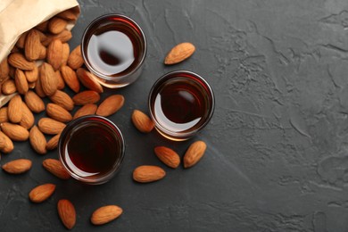 Photo of Glasses with tasty amaretto liqueur and almonds on dark gray table, flat lay. Space for text