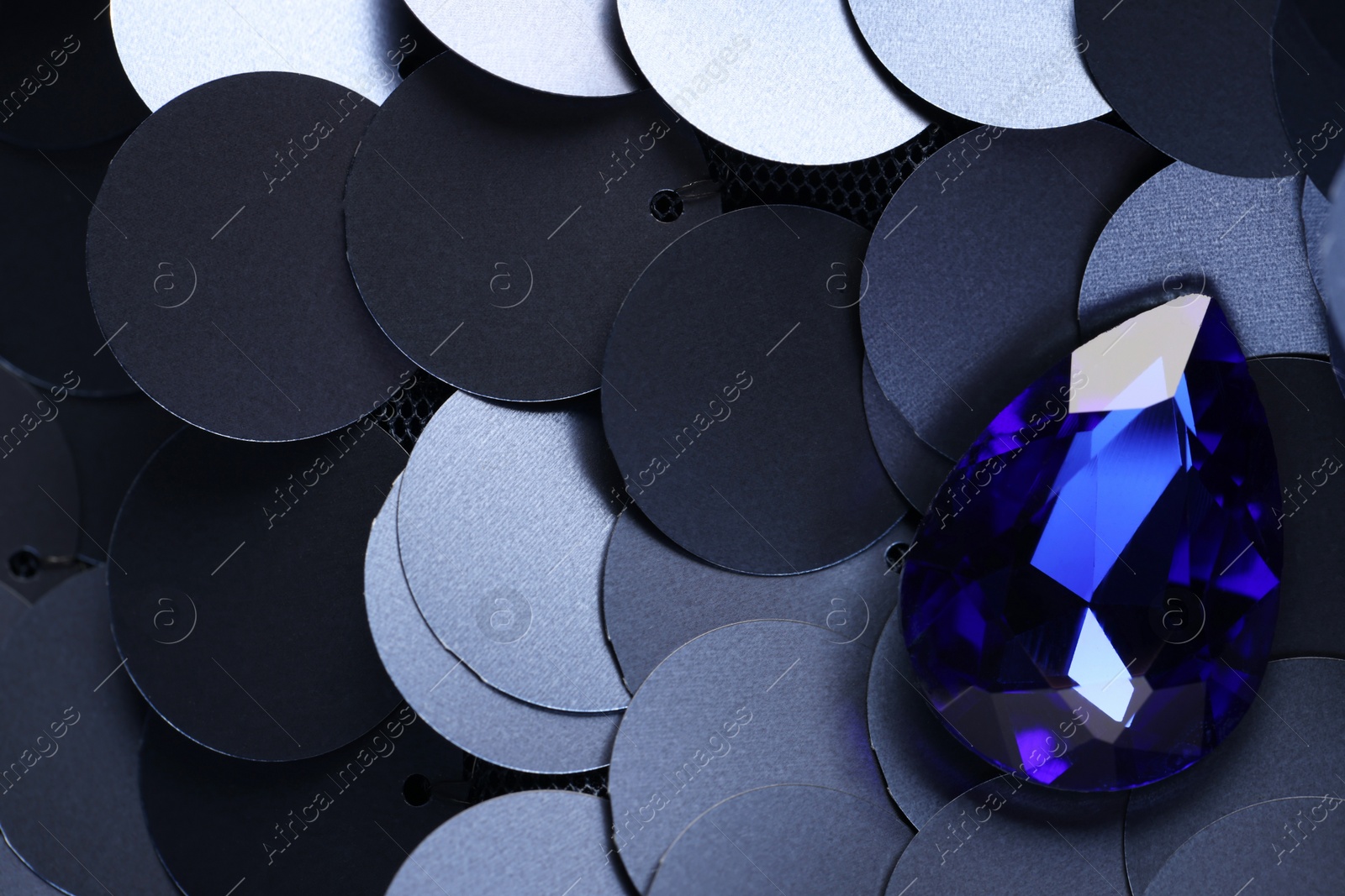 Photo of Beautiful blue gemstone for jewelry on sequin fabric, top view. Space for text