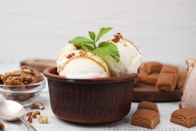 Photo of Bowl of tasty ice cream with caramel sauce, mint, nuts and candies on white wooden table, closeup