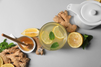 Photo of Delicious ginger tea and ingredients on light grey background, flat lay